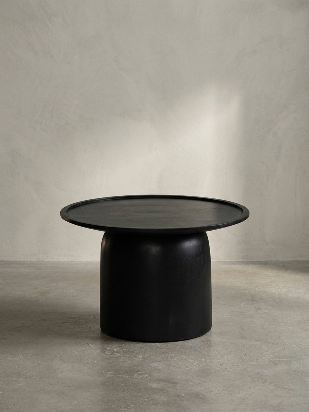 Frontansicht des runden, schwarzen Couchtisches aus massivem Mangoholz mit Trommelgestell auf weißem Hintergrund._