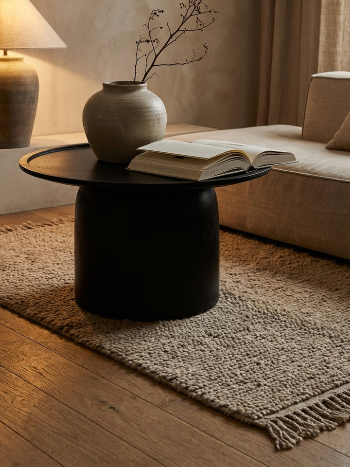 Ein schwarzer, runder Kaffeetisch mit erhöhtem Rand, auf dem ein Architekturbuch und eine Keramikvase stilvoll dekoriert sind._