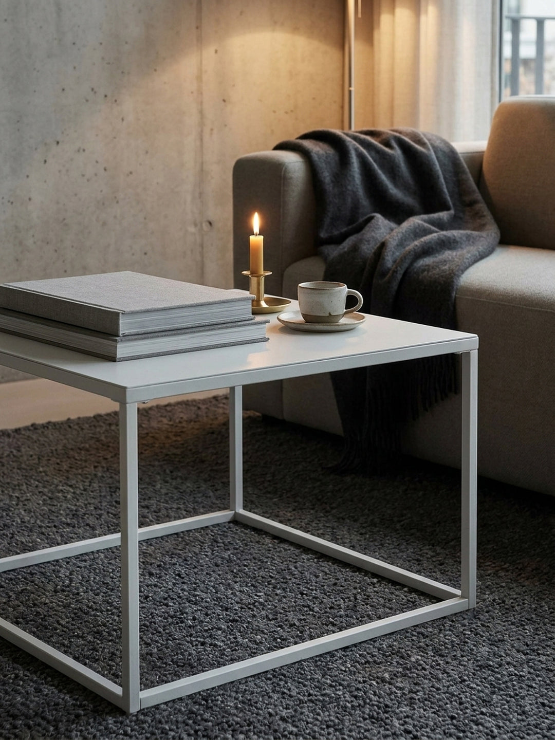 Weißer Industrial-Kaffeetisch aus Metall mit aufgeschlagenem Buch und Lesebrille arrangiert neben einem greige-farbenen Modulsofa_
