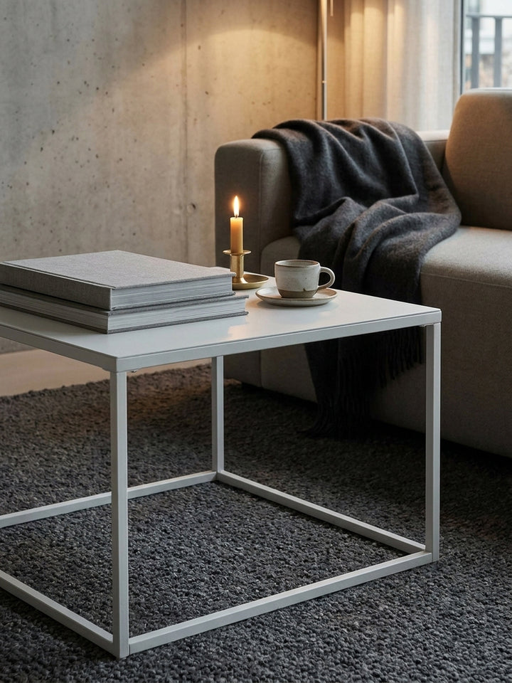 Weißer Industrial-Kaffeetisch aus Metall mit aufgeschlagenem Buch und Lesebrille arrangiert neben einem greige-farbenen Modulsofa_