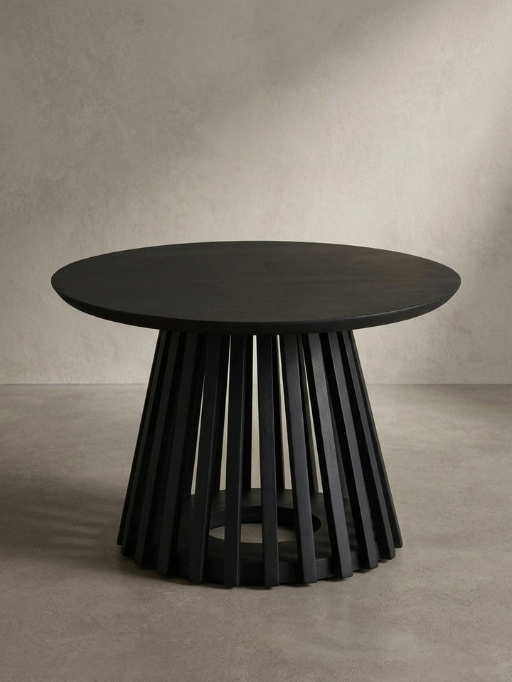 Freigestellte Frontansicht des runden Couchtischs in Schwarz, der die massive Tischplatte und das skulpturale Gittergestell aus Mangoholz zeigt._