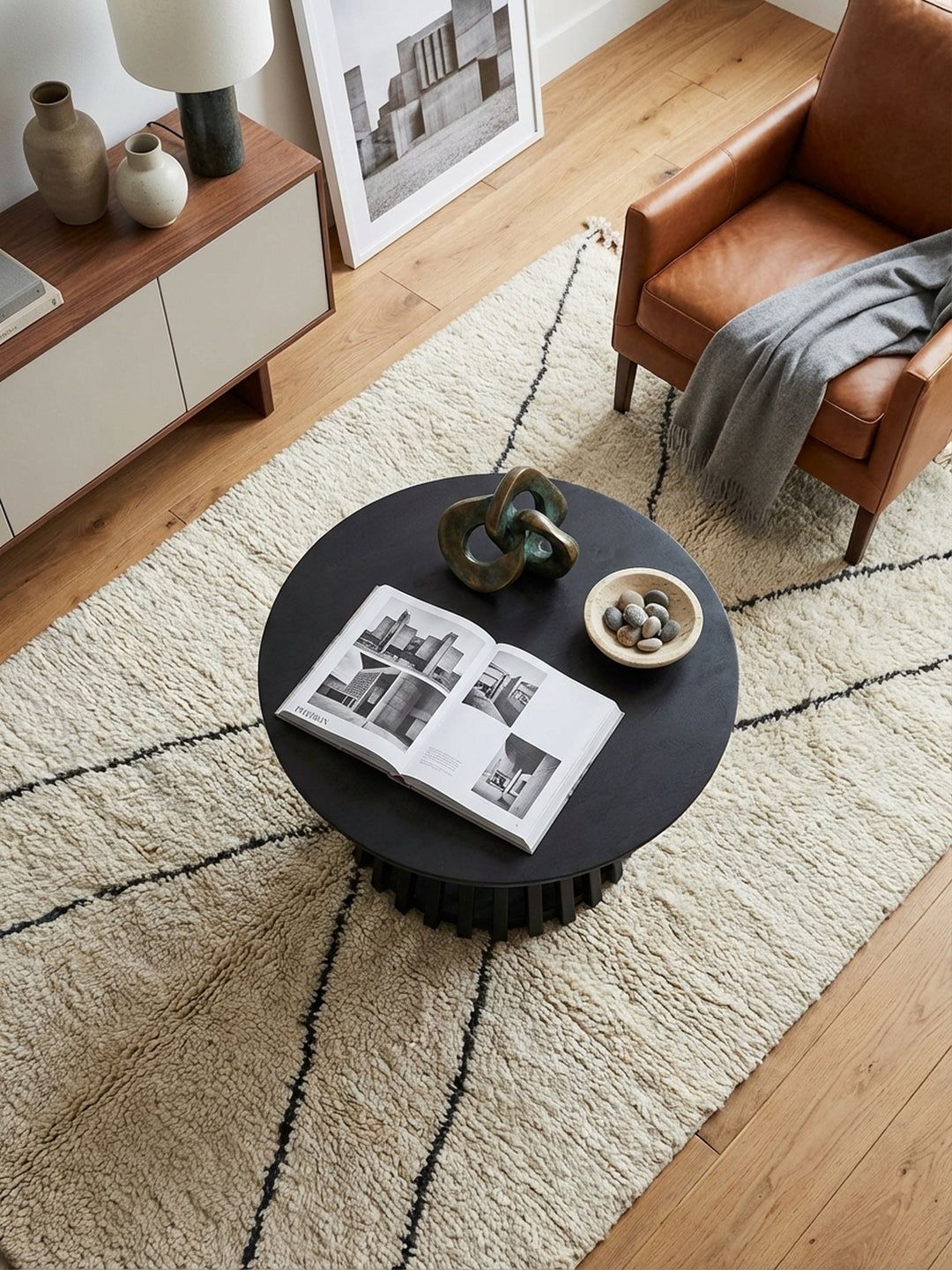 Aufsicht des schwarzen Design-Sofatischs mit Gittergestell, platziert auf einem elfenbeinfarbenen Wollteppich vor einer modernen Couch-Landschaft._