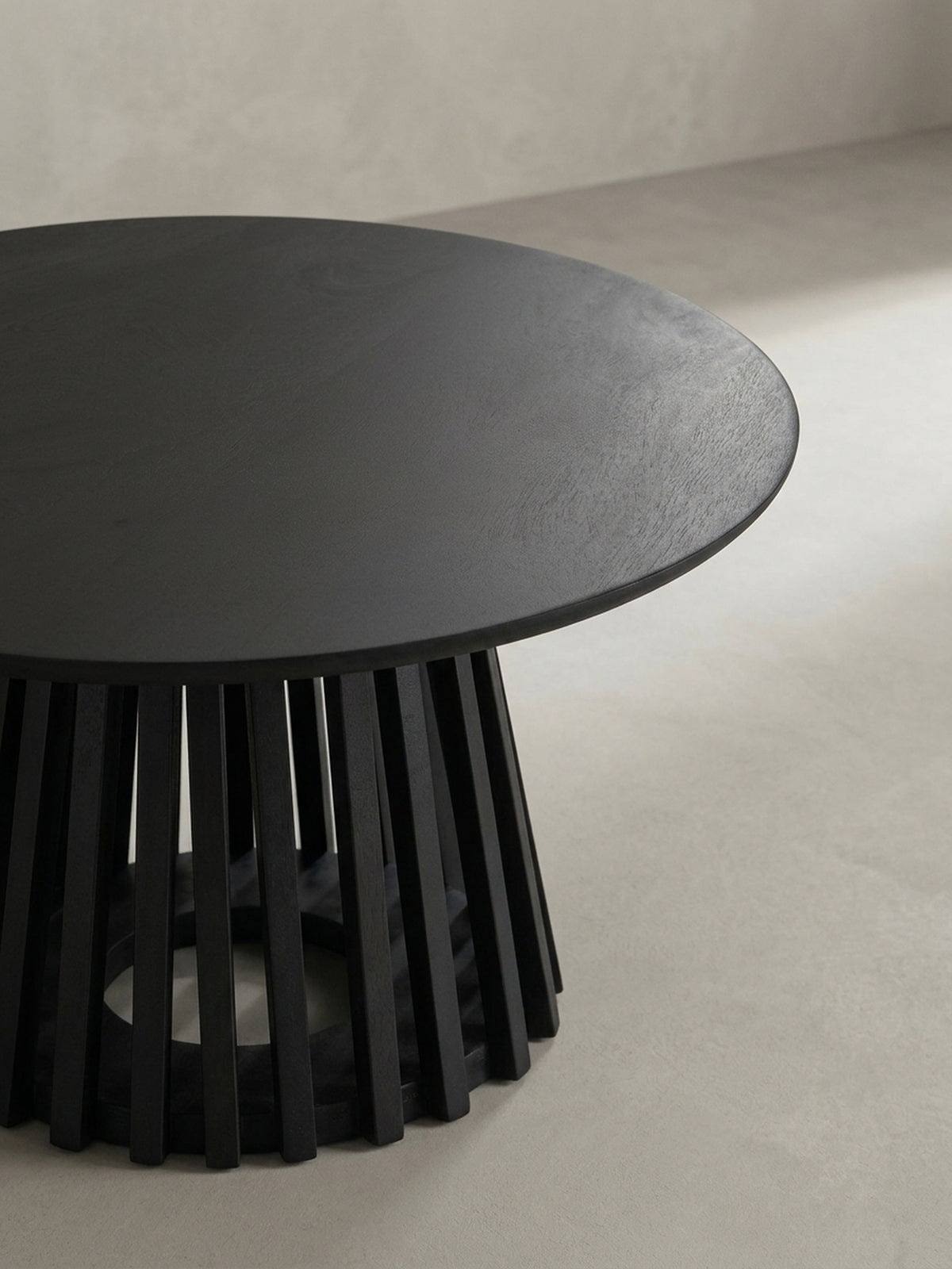 Alternativer Blickwinkel auf den schwarzen Couchtisch, der die Beziehung zwischen der glatten runden Platte und den vertikalen Lamellen des Fußes zeigt.