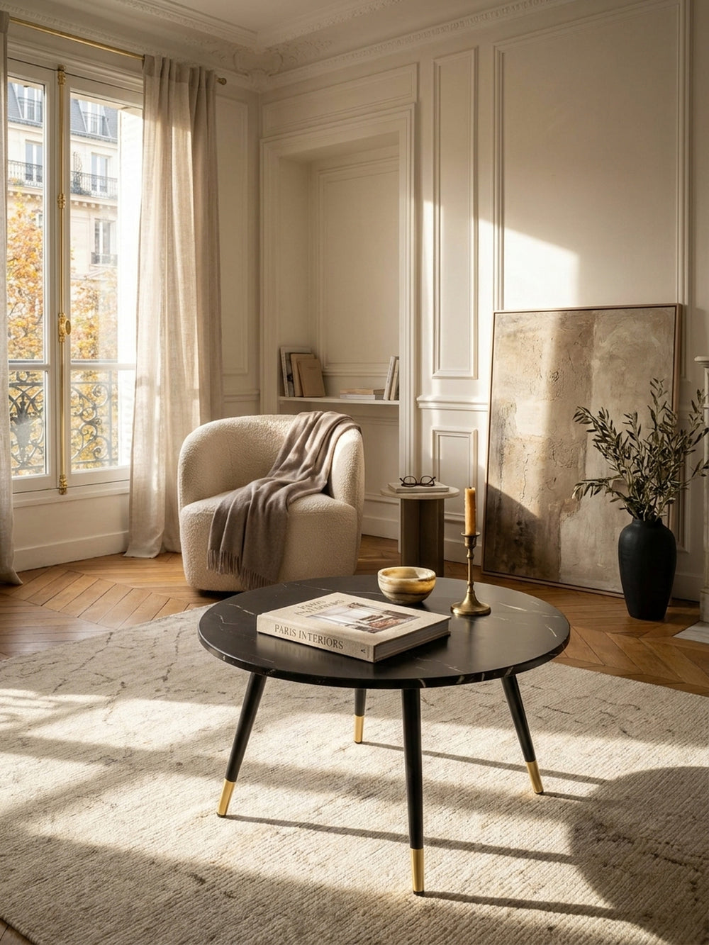 Großzügiges elegantes Wohnzimmer im Pariser Stil mit einem runden Couchtisch in schwarzer Marmoroptik vor warmweißer Boiserie auf edlem Fischgrätparkett._