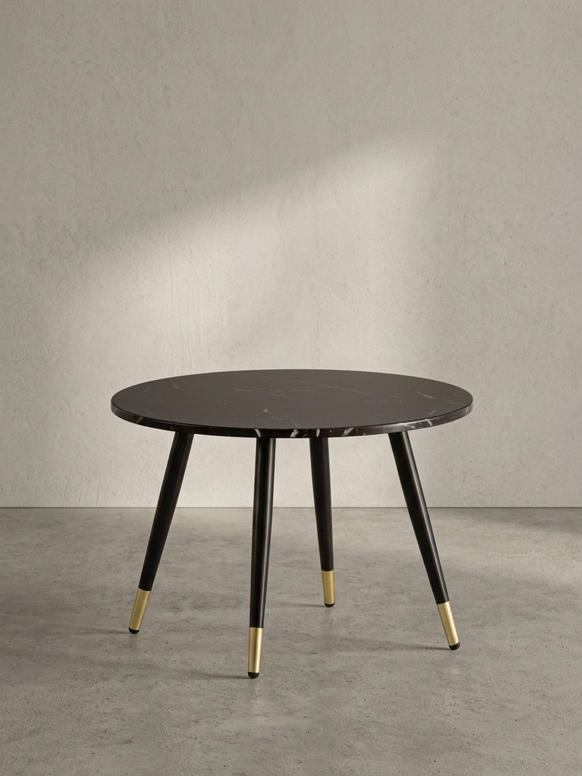 Freigestellter runder Couchtisch mit einer 60 cm breiten dunklen Marmor-Dekor-Platte und konisch zulaufenden schwarzen Metallbeinen.
