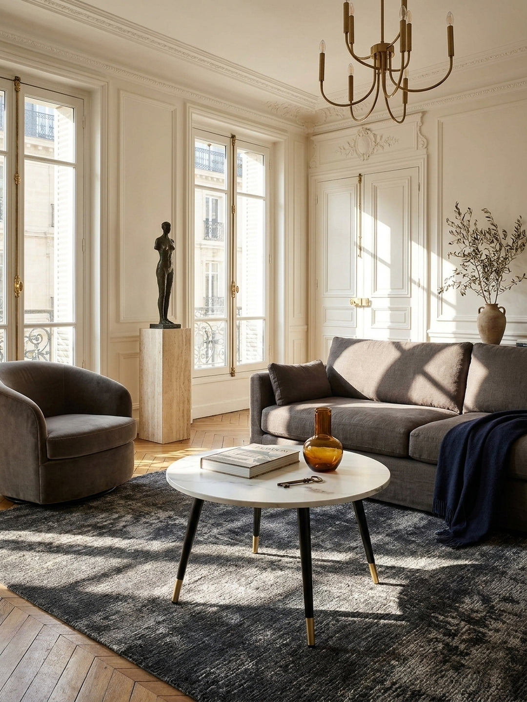 Runder Couchtisch mit weißer Marmoroptik und schwarz-goldenen Metallbeinen im eleganten Pariser Wohnzimmer mit Fischgrätparkett_