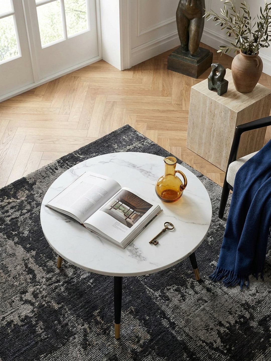 Draufsicht auf einen kleinen 60x60 cm Wohnzimmertisch in edler Marmoroptik arrangiert neben einem dunklen Samtsofa auf anthrazitfarbenem Teppich_
