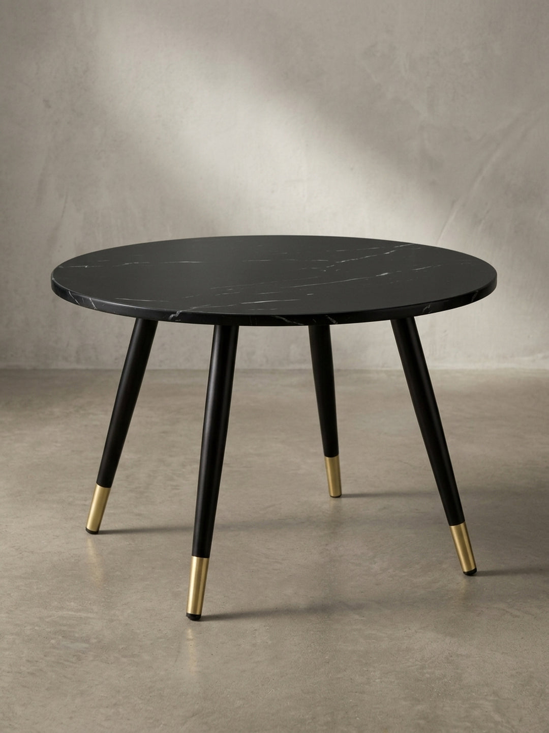 Eleganter Design-Couchtisch schräg von der Seite betrachtet mit Fokus auf die kontrastierenden filigranen Füße mit glänzenden Messingkappen._
