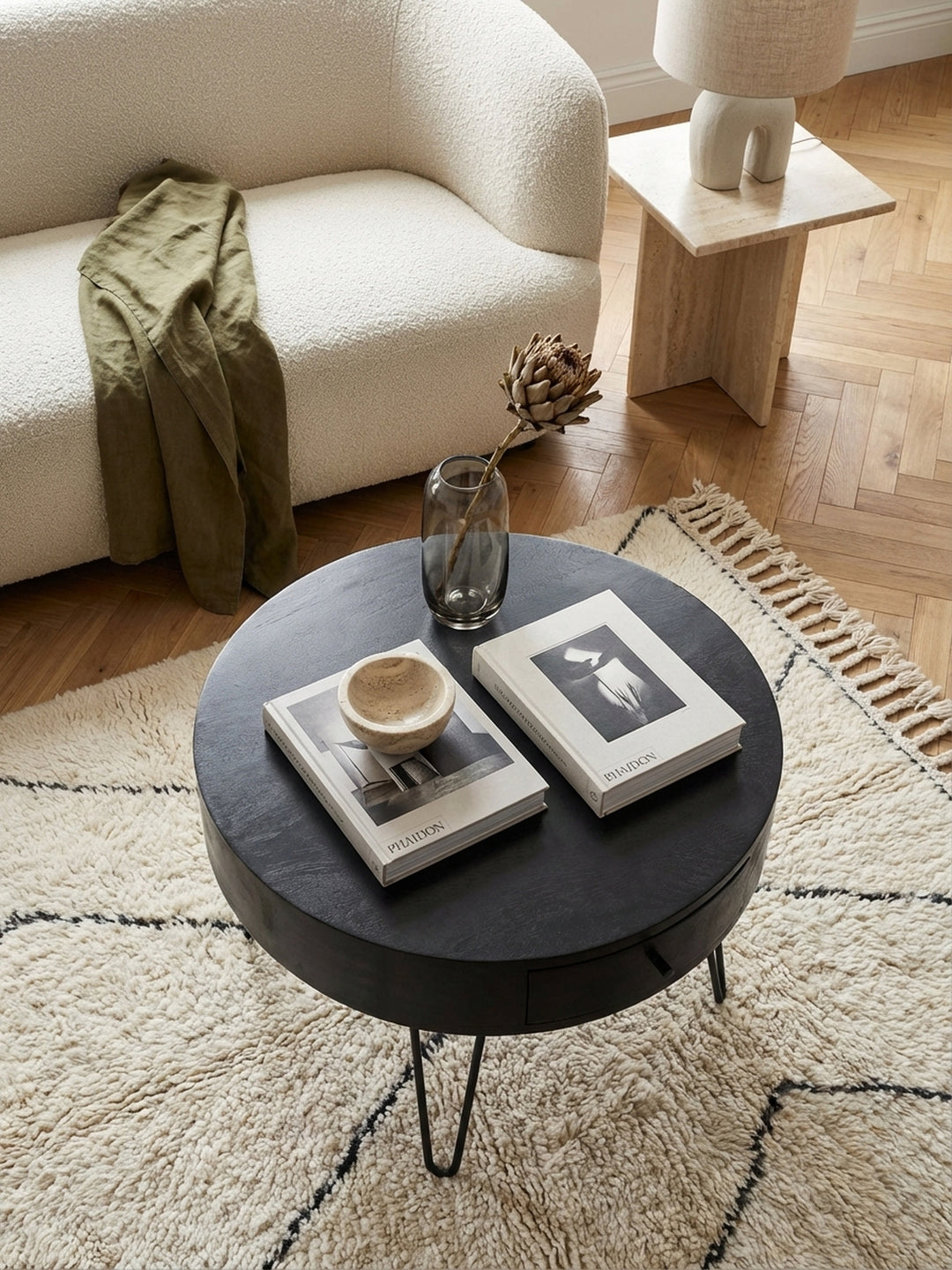 Blick von oben auf den schwarzen Design-Couchtisch mit Haarnadelbeinen, der eine harmonische Einheit mit einem hellen Sofa und einem gemusterten Teppich bildet._