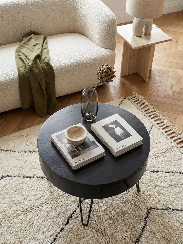 Blick von oben auf den schwarzen Design-Couchtisch mit Haarnadelbeinen, der eine harmonische Einheit mit einem hellen Sofa und einem gemusterten Teppich bildet._