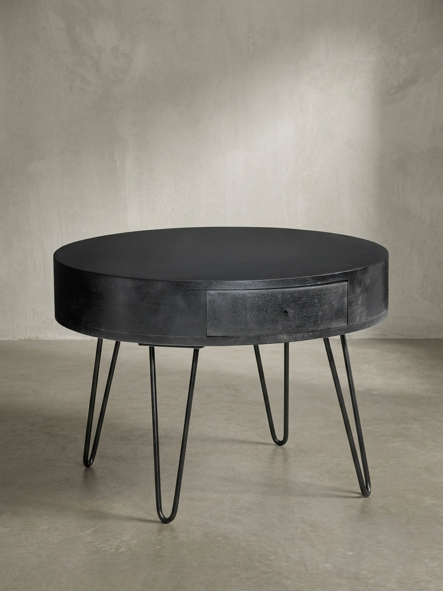 Dreiviertelansicht des massiven Couchtischs aus Mangoholz, der die Kombination aus dem runden Korpus und den schlanken Metallbeinen hervorhebt._