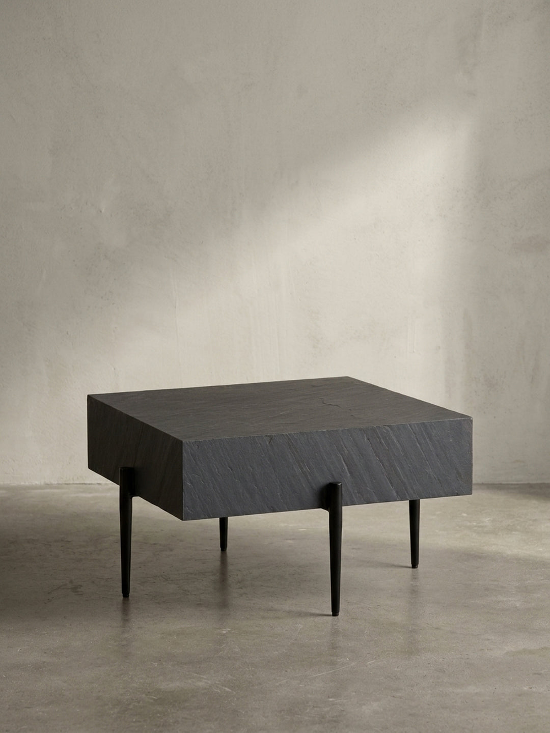 Freigestellter quadratischer Couchtisch in Anthrazit mit strukturierter Steinoptik-Platte und schlanken, schwarzen Metallbeinen vor weißem Hintergrund._