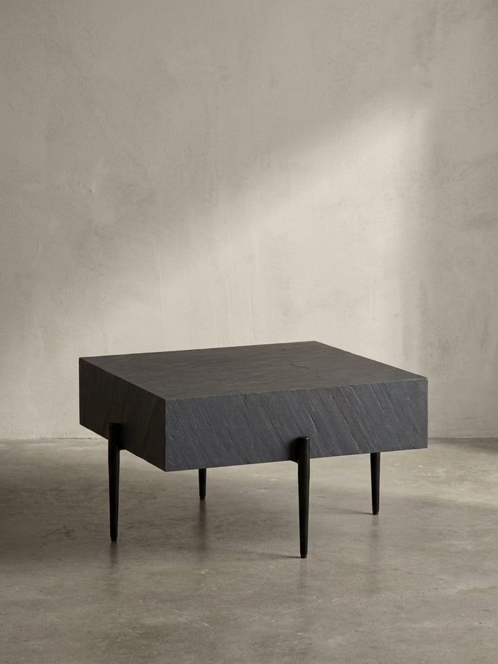 Freigestellter quadratischer Couchtisch in Anthrazit mit strukturierter Steinoptik-Platte und schlanken, schwarzen Metallbeinen vor weißem Hintergrund._