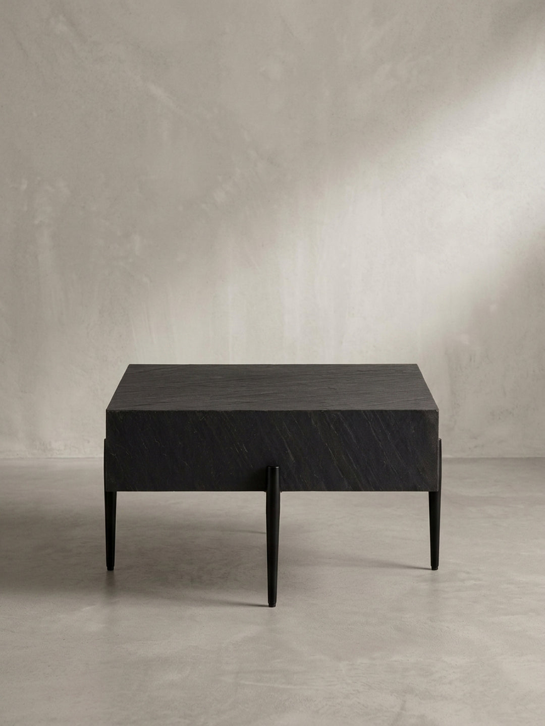 Design-Couchtisch aus der Dreiviertel-Perspektive, der die schwebende Optik der massiven Tischplatte über den filigranen Metallbeinen hervorhebt._