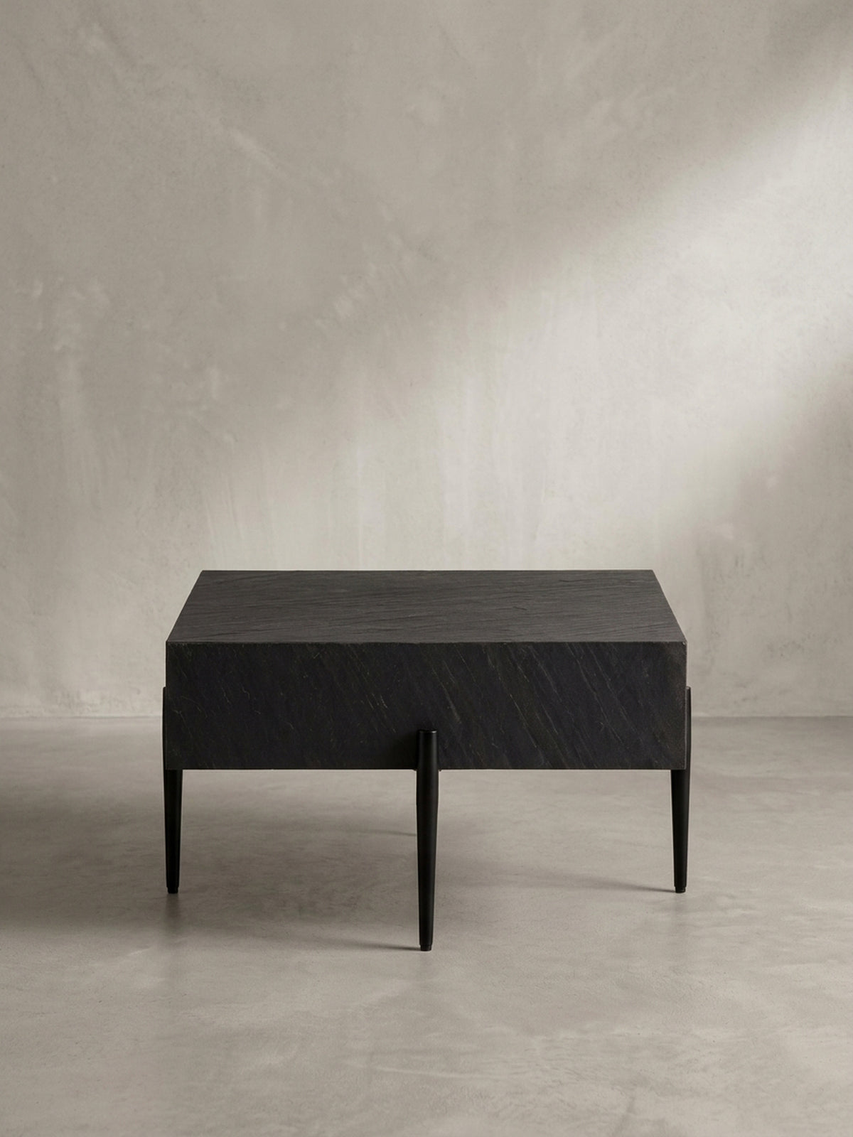 Design-Couchtisch aus der Dreiviertel-Perspektive, der die schwebende Optik der massiven Tischplatte über den filigranen Metallbeinen hervorhebt._