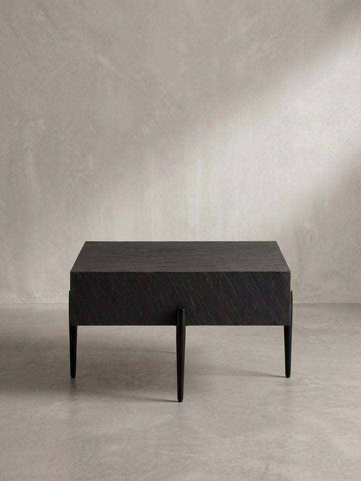 Design-Couchtisch aus der Dreiviertel-Perspektive, der die schwebende Optik der massiven Tischplatte über den filigranen Metallbeinen hervorhebt._