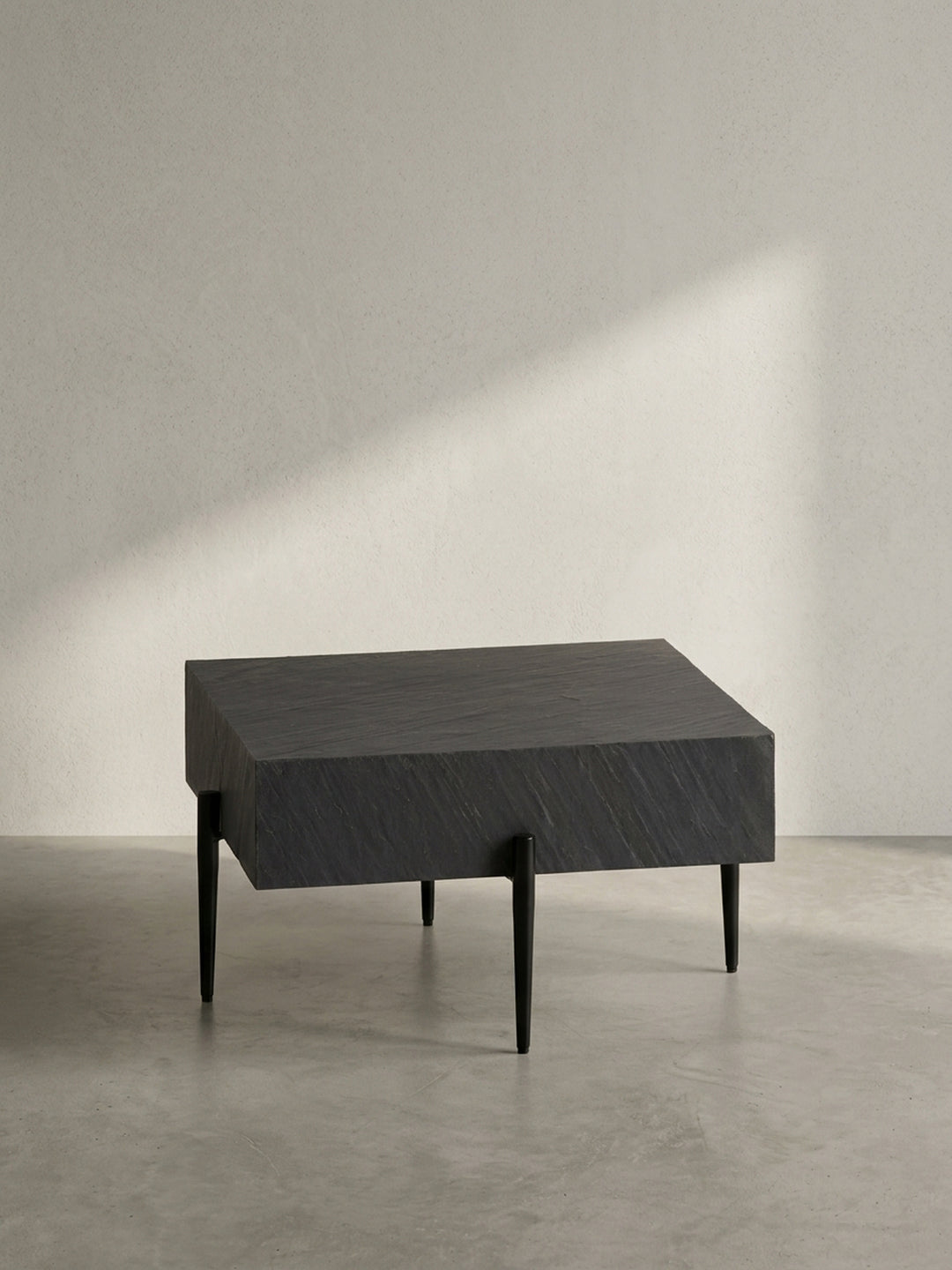 Seitenansicht des modernen Sofatischs, die das Kontrastspiel zwischen der 15 cm dicken Platte in Steinoptik und den grazilen, konischen Beinen zeigt._