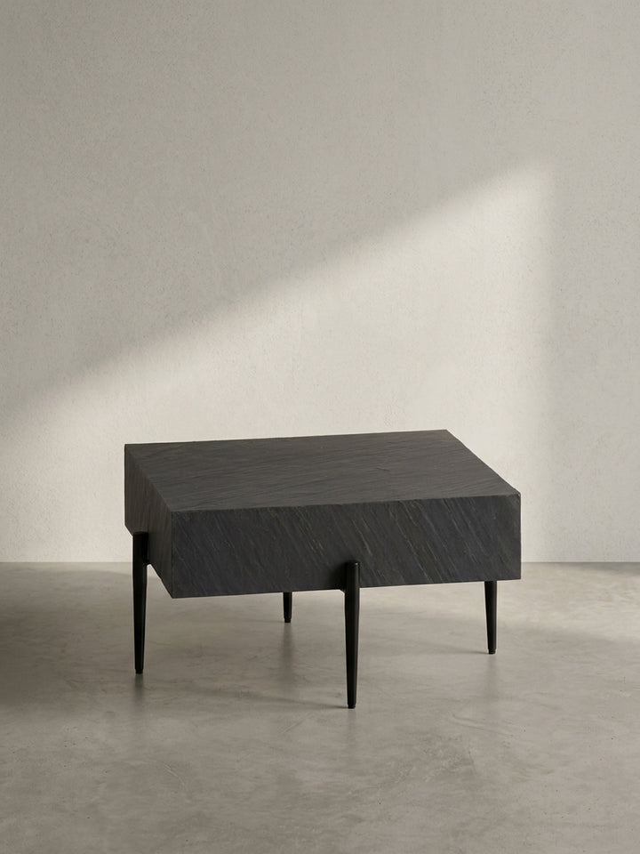 Seitenansicht des modernen Sofatischs, die das Kontrastspiel zwischen der 15 cm dicken Platte in Steinoptik und den grazilen, konischen Beinen zeigt._