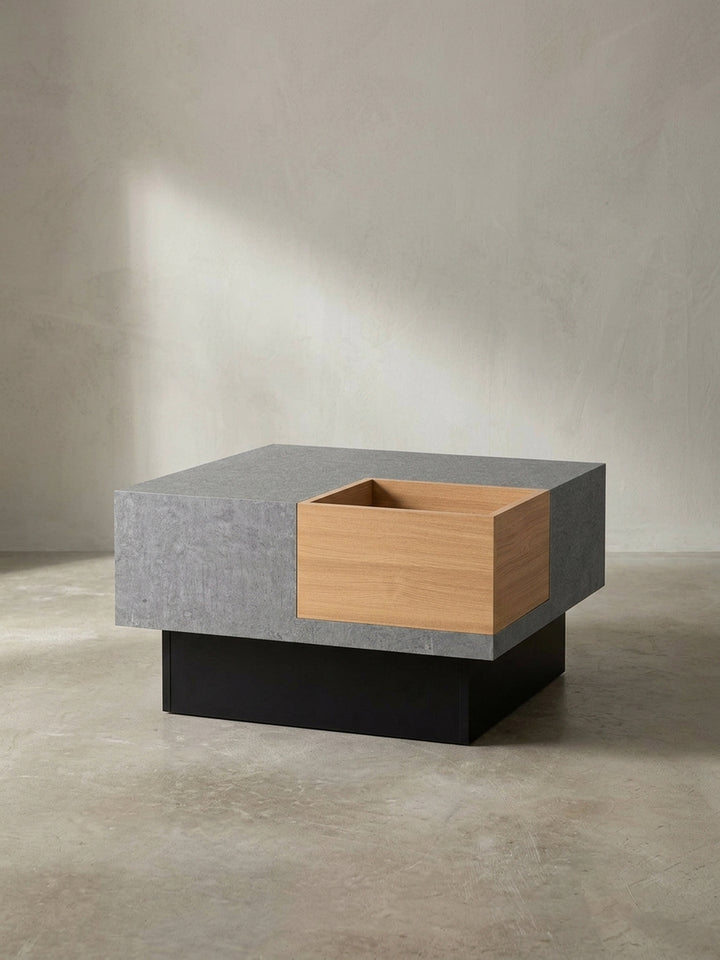Quadratischer Couchtisch 65x65x40 cm in strukturierter Beton-Optik mit schwarzem Sockel und eichefarbenem Fach freigestellt vor weißem Hintergrund._