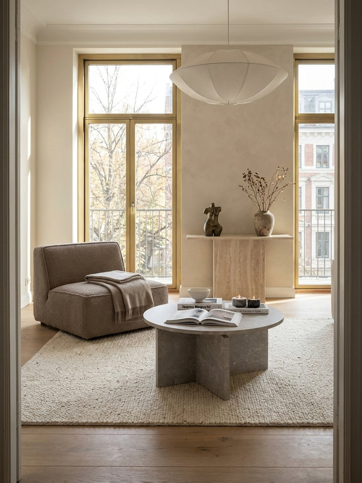 Skulpturaler Couchtisch in sandfarbener Stein-Optik 60x60 cm als Herzstück in einem luxuriösen organisch-modernen Wohnzimmer mit beigem Bouclé-Sofa und echten Eichendielen._