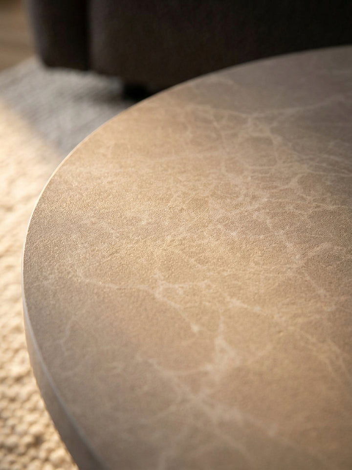 Nahaufnahme der täuschend echten Stein-Optik des MDF-Couchtisches, die eine feine Marmorierung und eine angenehm warme, beige-sandfarbene Oberfläche zeigt._