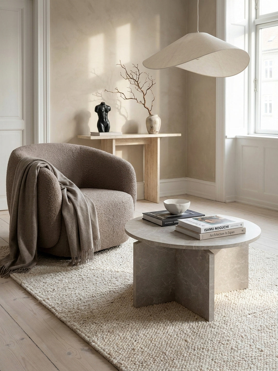 Sandfarbener Kaffeetisch elegant kombiniert mit einem cremeweißen Leinen-Sofa und einem dunklen, voluminösen Kaschmir-Plaid in einer stilvollen Architektenwohnung._