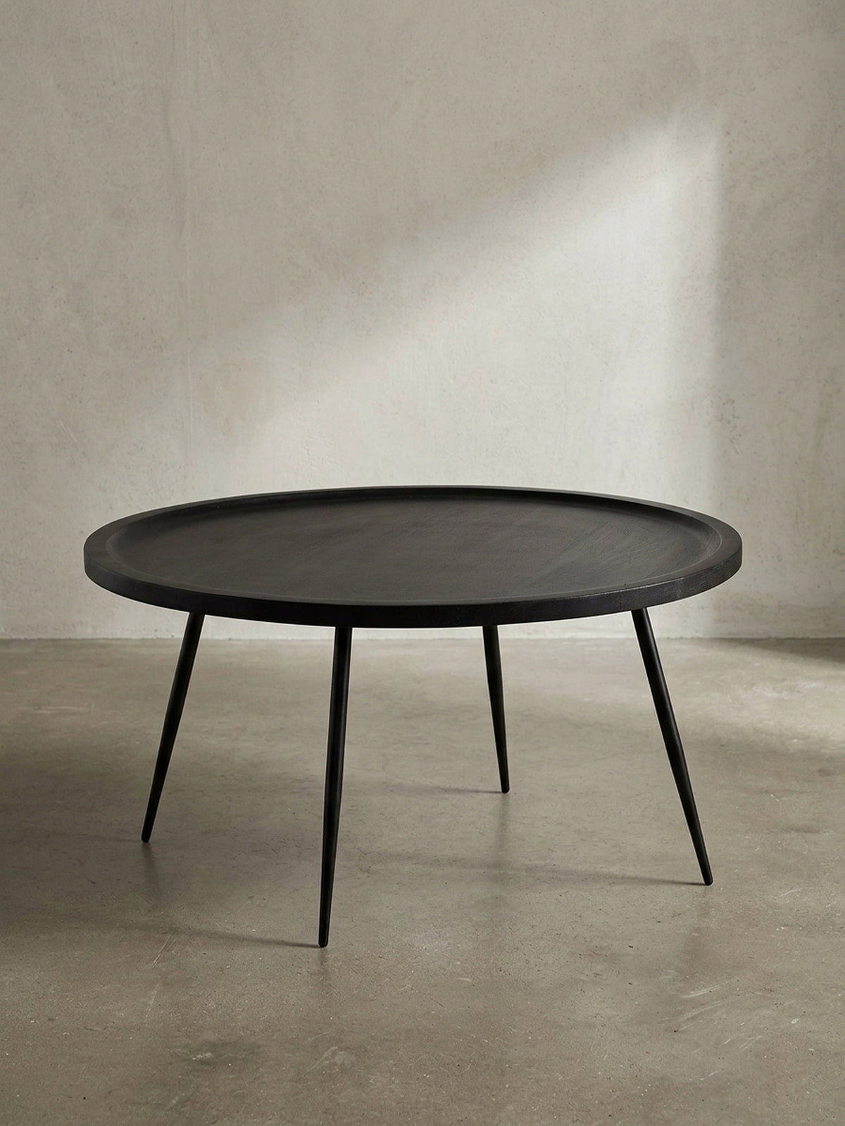 Freigestellte Frontansicht des runden Couchtischs aus massivem Mangoholz in Schwarz mit vier filigranen Metallbeinen vor weißem Hintergrund._