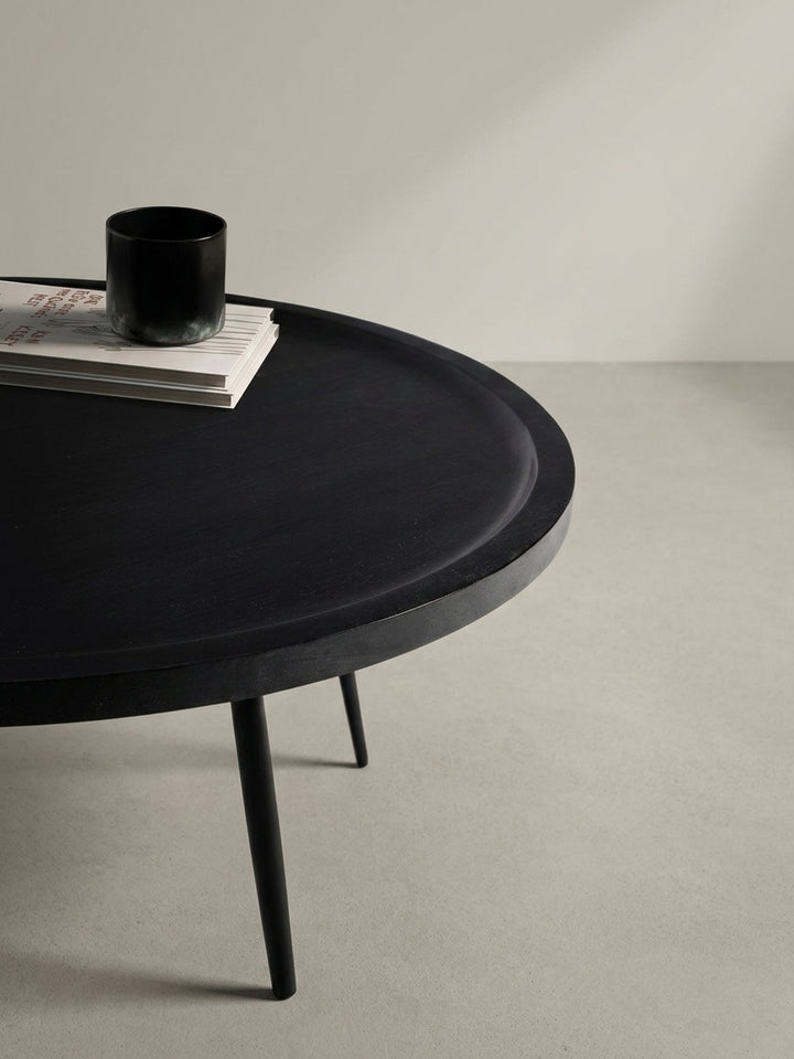 Der runde Kaffeetisch aus schwarzem Massivholz und Eisen aus einer anderen Perspektive, die die leicht erhöhte Kante der Tischplatte hervorhebt._