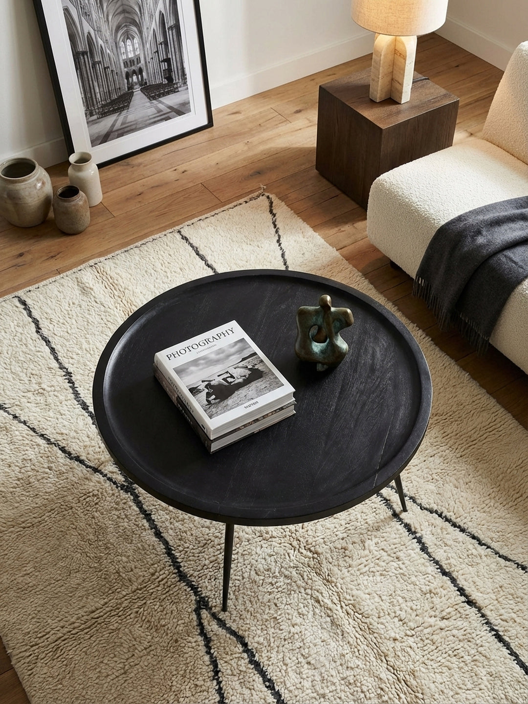 Runder Sofatisch aus schwarzem Mangoholz von oben, arrangiert auf einem hellen Teppich vor einer modernen Couch – perfekt für ein stilvolles Ambiente._