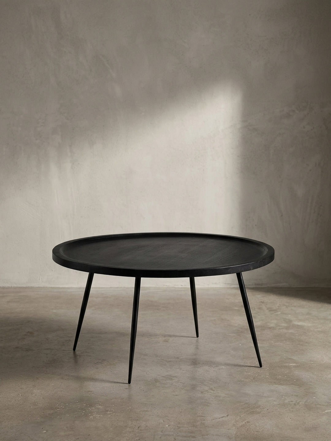 Schräger Blick auf den zeitlosen Sofatisch mit runder Platte aus schwarzem Mangoholz, der seine elegante Form und das schlanke Beingestell betont._