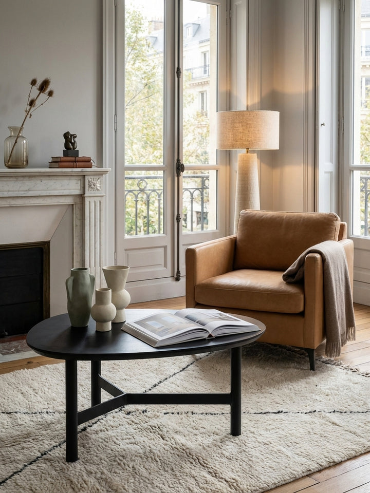 Der dreibeinige Kaffeetisch in Schwarz harmoniert perfekt mit einem cremefarbenen Sofa und einem gemusterten Teppich und schafft so ein modernes und stimmiges Wohnambiente._