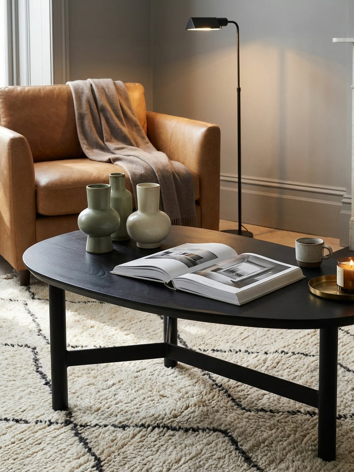 Eine klare Glasvase und ein Holztablett stehen auf dem nierenförmigen Sofatisch aus schwarzem Holz und schaffen eine gemütliche Atmosphäre im Wohnzimmer._