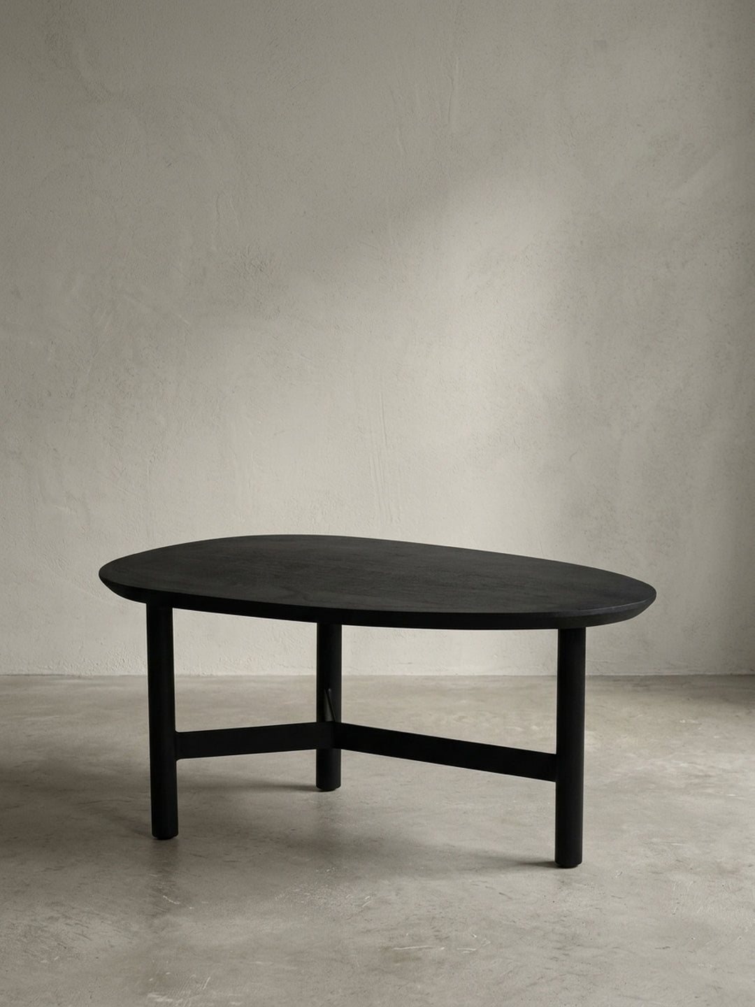 Frontansicht des modernen Couchtischs in Nierenform aus massivem Mangoholz in Schwarz, freigestellt vor weißem Hintergrund, um die skulpturale Form zu zeigen._