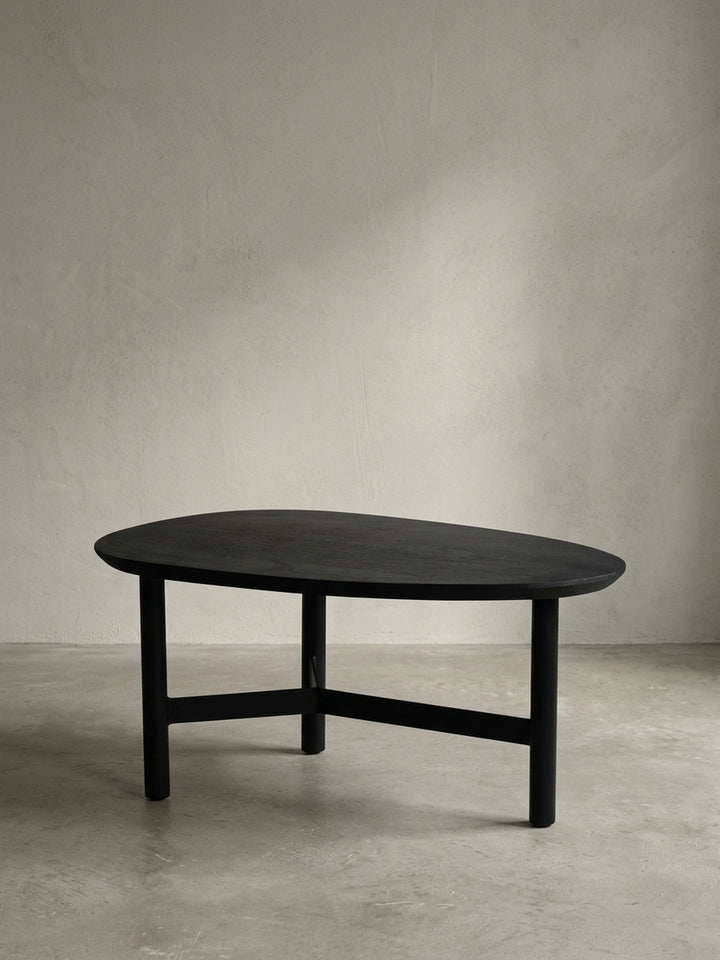 Frontansicht des modernen Couchtischs in Nierenform aus massivem Mangoholz in Schwarz, freigestellt vor weißem Hintergrund, um die skulpturale Form zu zeigen._