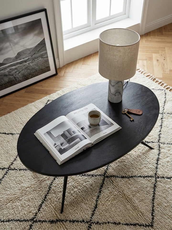 Draufsicht auf den schwarzen ovalen Sofatisch 90x50x35 cm mit sichtbarer Holzmaserung arrangiert auf einem hellen Teppich neben einer modernen Couchlandschaft_