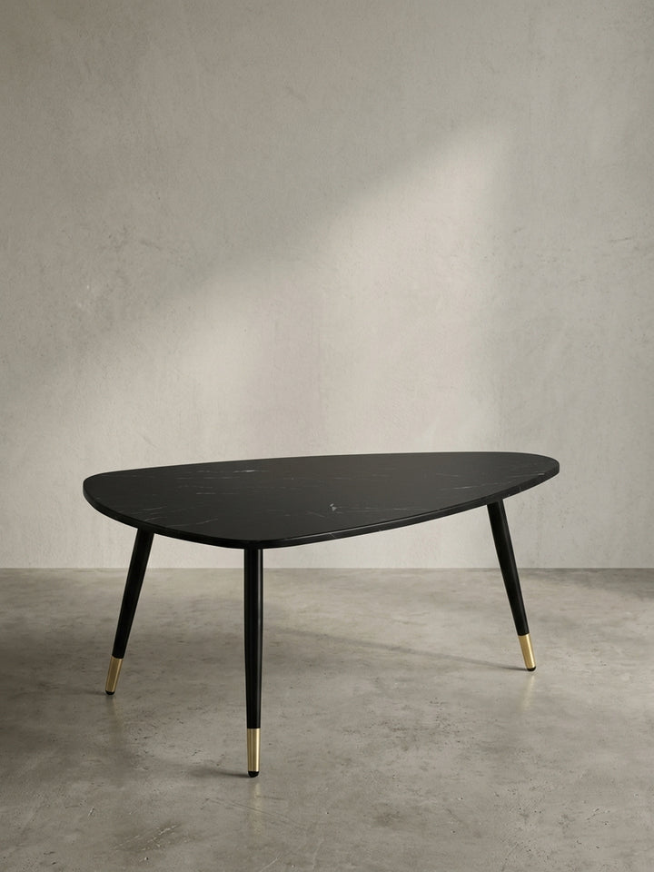 Gesamtübersicht des dreieckigen Wohnzimmertisches 90x60x41 cm, der eine stilvolle Balance aus schwarzer Steinoptik und warmen Messingdetails bietet._
