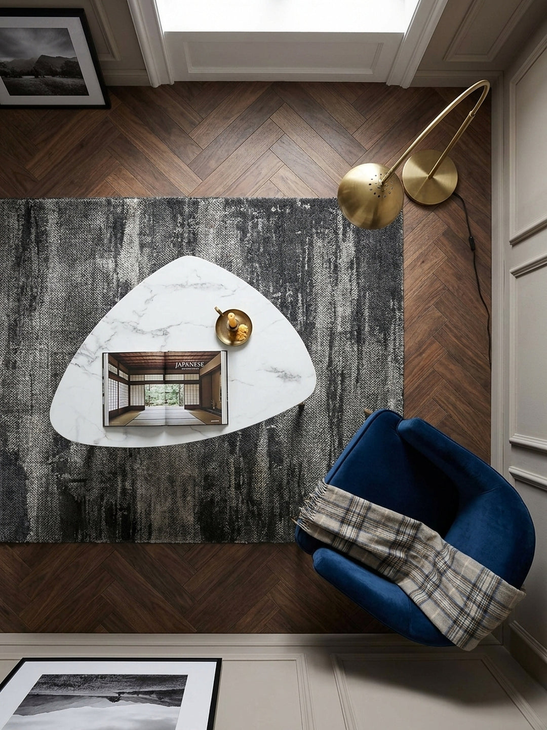Draufsicht auf den dreieckigen Wohnzimmertisch 90x60 cm mit schwarzen Beinen und goldenen Akzenten neben einem dunkelblauen Samtsessel._