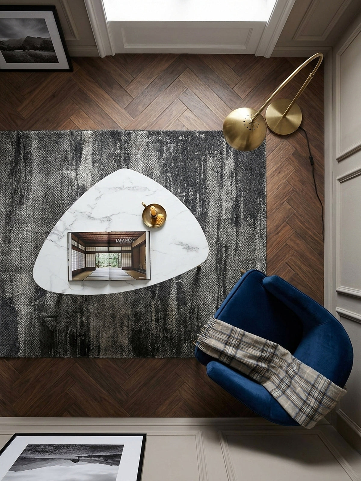 Draufsicht auf den dreieckigen Wohnzimmertisch 90x60 cm mit schwarzen Beinen und goldenen Akzenten neben einem dunkelblauen Samtsessel._