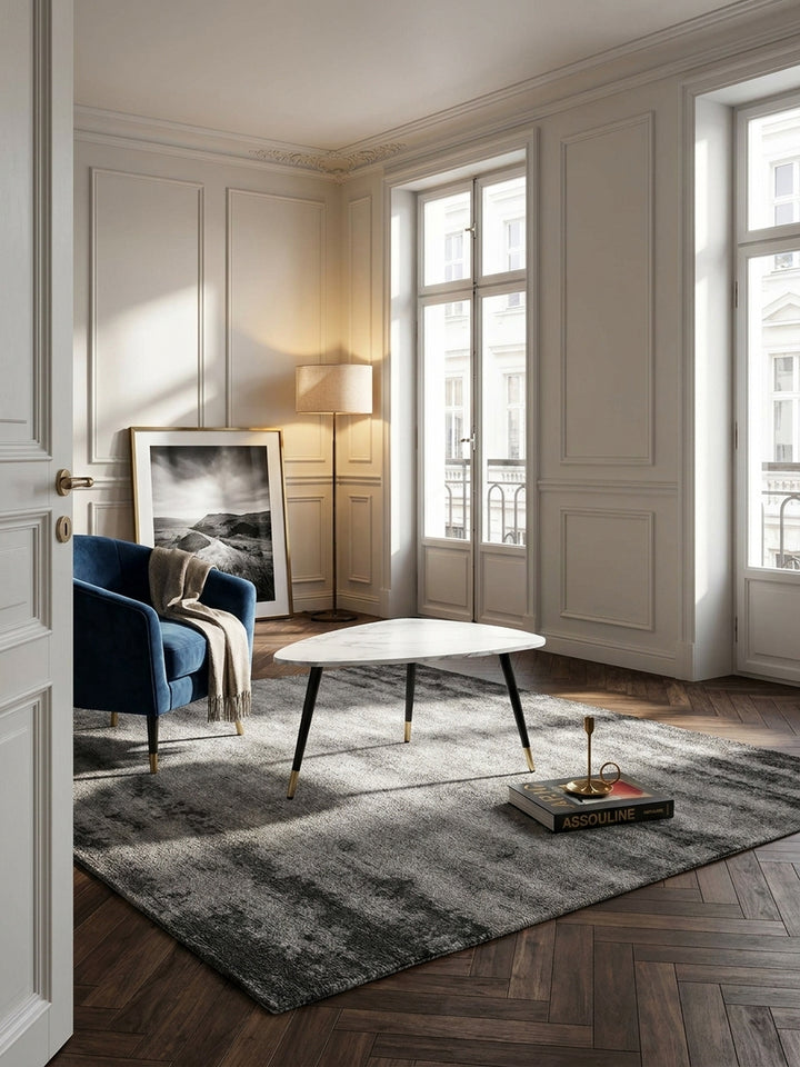 Eleganter Couchtisch in weißer Marmor-Optik auf dunklem Fischgrätparkett in einem stilvollen Pariser Wohnzimmer mit hohen Decken._