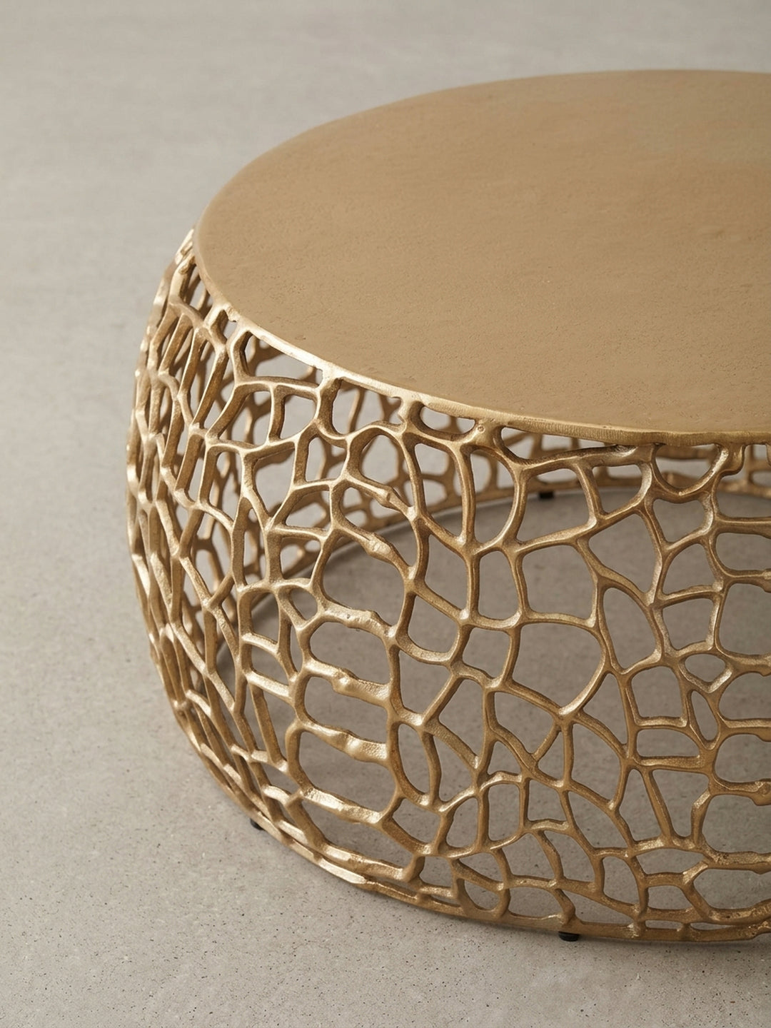 Perspektivische Ansicht des runden Beistelltischs in Gold, die das Zusammenspiel von Licht und Schatten auf der komplexen, netzartigen Metallstruktur einfängt._