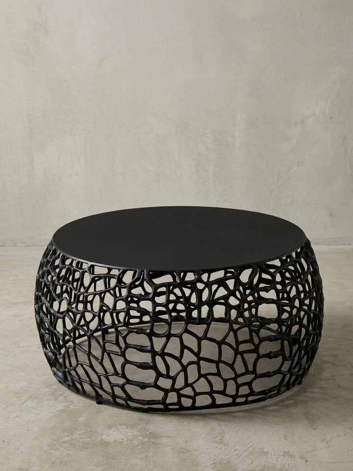 Seitenansicht des modernen Kaffeetischs aus schwarzem Aluminium, die niedrige Höhe von 30 cm und die Proportionen des runden Sofatischs sind klar ersichtlich._