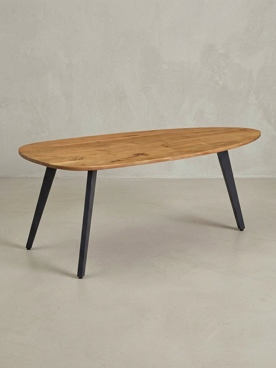 Design-Sofatisch 110 cm lang in einer dynamischen Dreiviertelansicht, die die asymmetrische Form der Massivholzplatte und die schrägen Tischbeine betont._