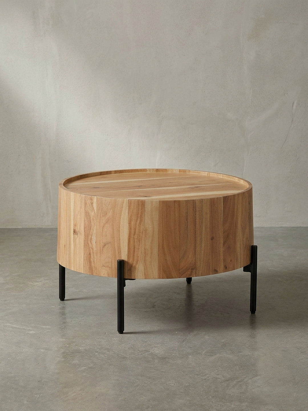 Frontalansicht des runden Couchtisches aus massivem Akazienholz mit seinem charakteristischen Trommelkorpus und den filigranen, schwarzen Metallbeinen vor weißem Hintergrund._