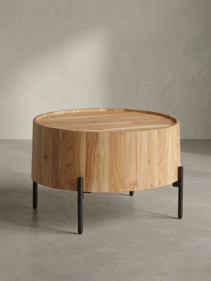 Seitenansicht des kleinen Sofatisches, die die schlanke Silhouette der schwarzen Metallbeine im Kontrast zum voluminösen Holzkörper aus Akazie zeigt._