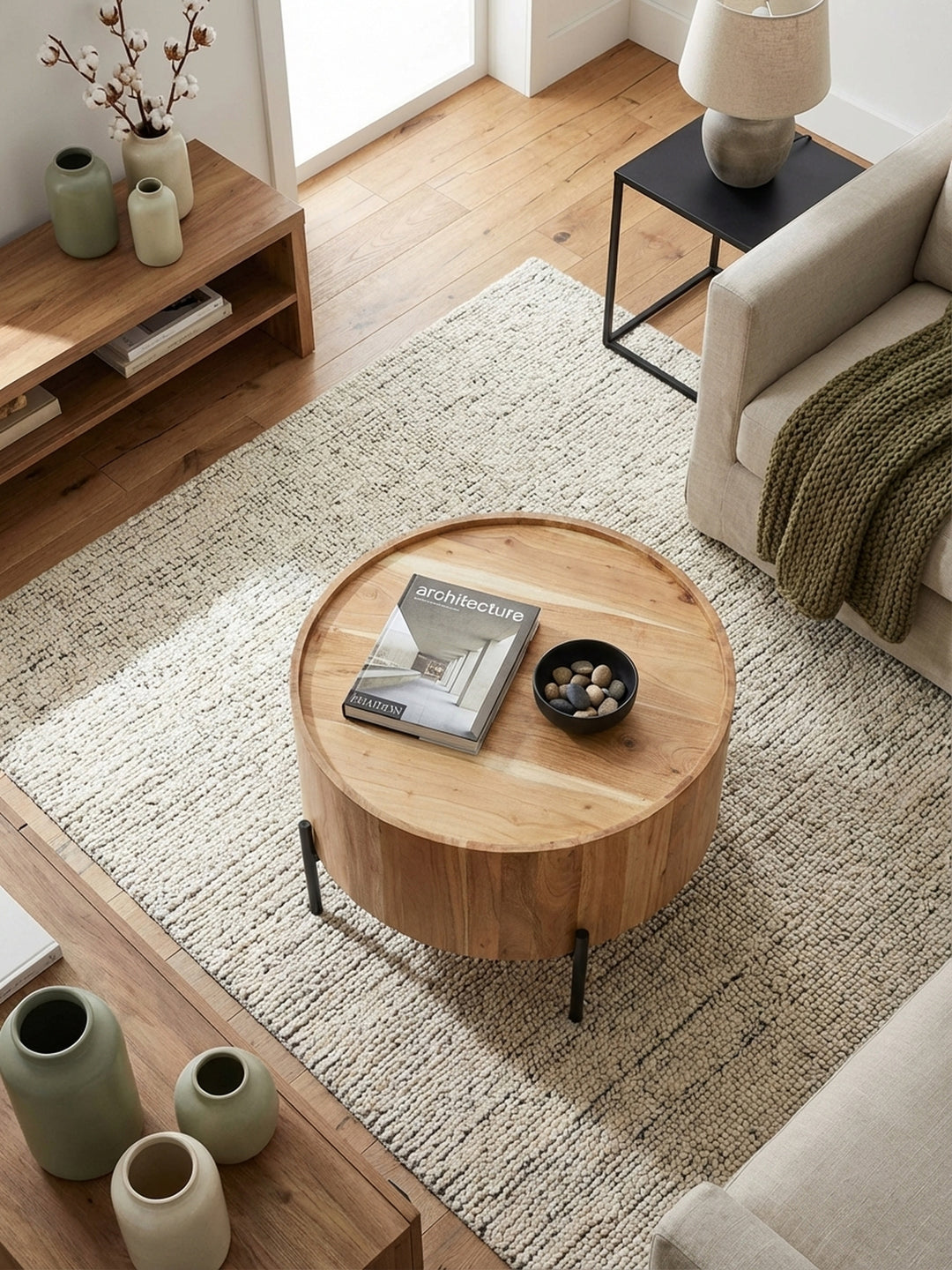 Von oben betrachtet, zeigt der Akazien-Couchtisch seine runde Form und die Holzmaserung, harmonisch arrangiert mit einem hellen Sofa und einem gemusterten Wollteppich._