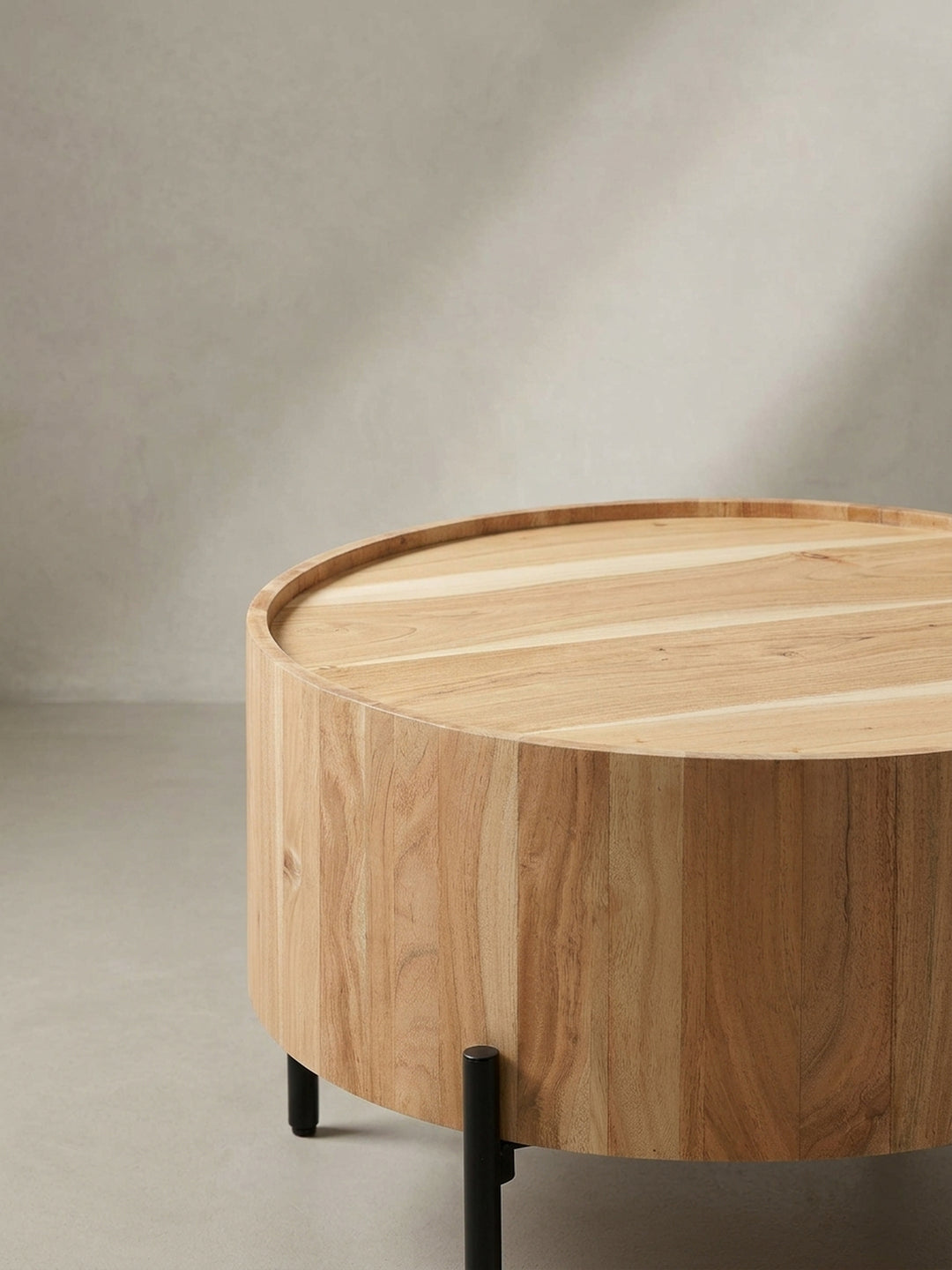 Schräge Ansicht des runden Kaffeetisches, die das Zusammenspiel von der warmen Holzfarbe der Akazie und dem mattschwarzen Metallgestell betont._