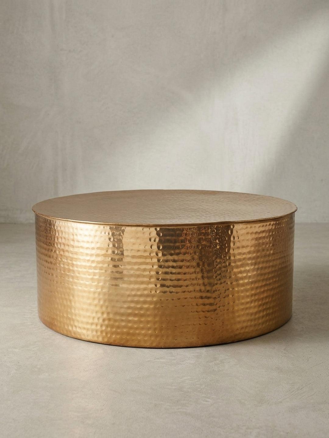 Runder Couchtisch aus goldenem Aluminium in zylindrischer Trommelform mit markantem Hammerschlag-Muster auf weißem Hintergrund._