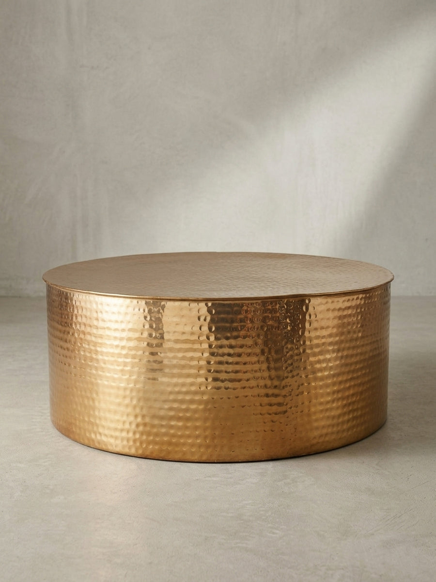 Runder Couchtisch aus goldenem Aluminium in zylindrischer Trommelform mit markantem Hammerschlag-Muster auf weißem Hintergrund._
