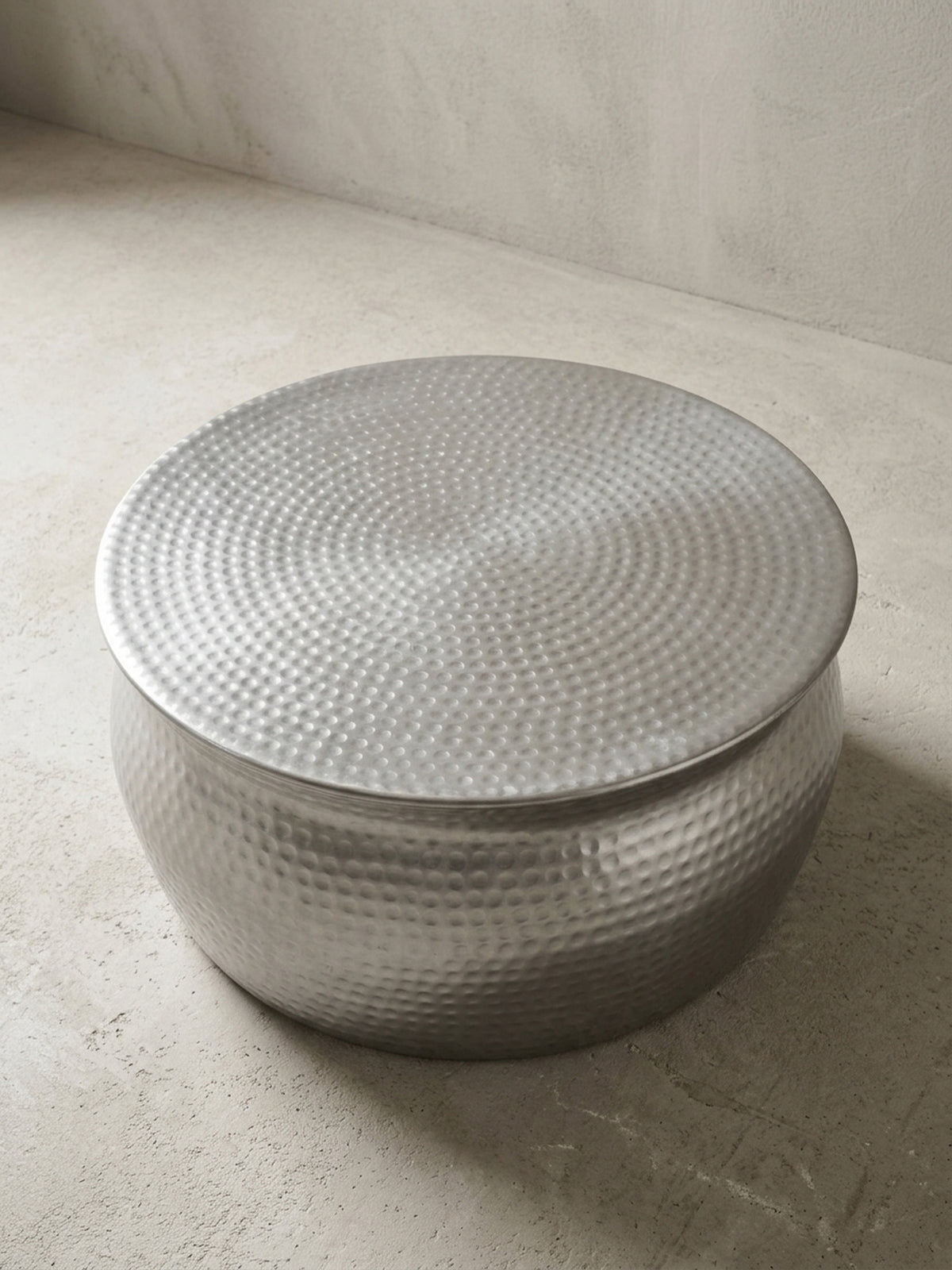Alternative Perspektive des flachen Aluminium-Tisches im Hammerschlag-Design. Das Lichtspiel auf der silbernen Oberfläche betont die organische, handgefertigte Form des Möbels.
