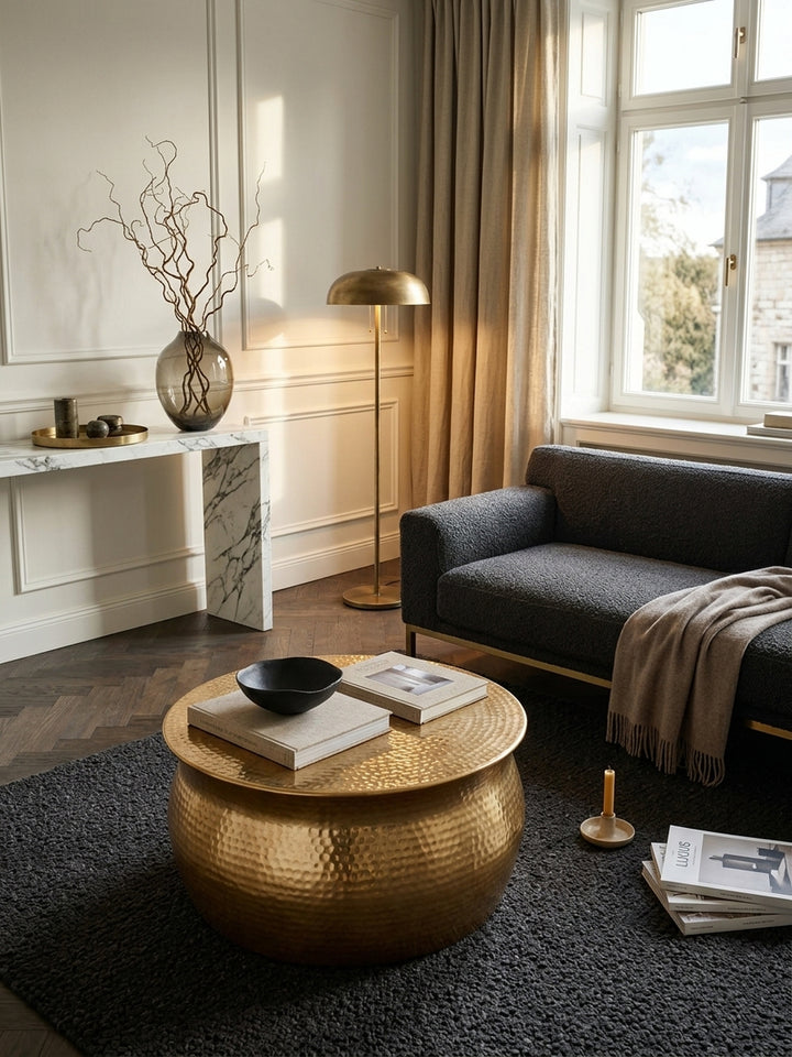 Aufsicht auf den runden goldenen Wohnzimmertisch im Modern-Classic Design. Die strukturierte Hammerschlag-Oberfläche des flachen 60cm Sofatisches reflektiert warmes Licht im Raum._